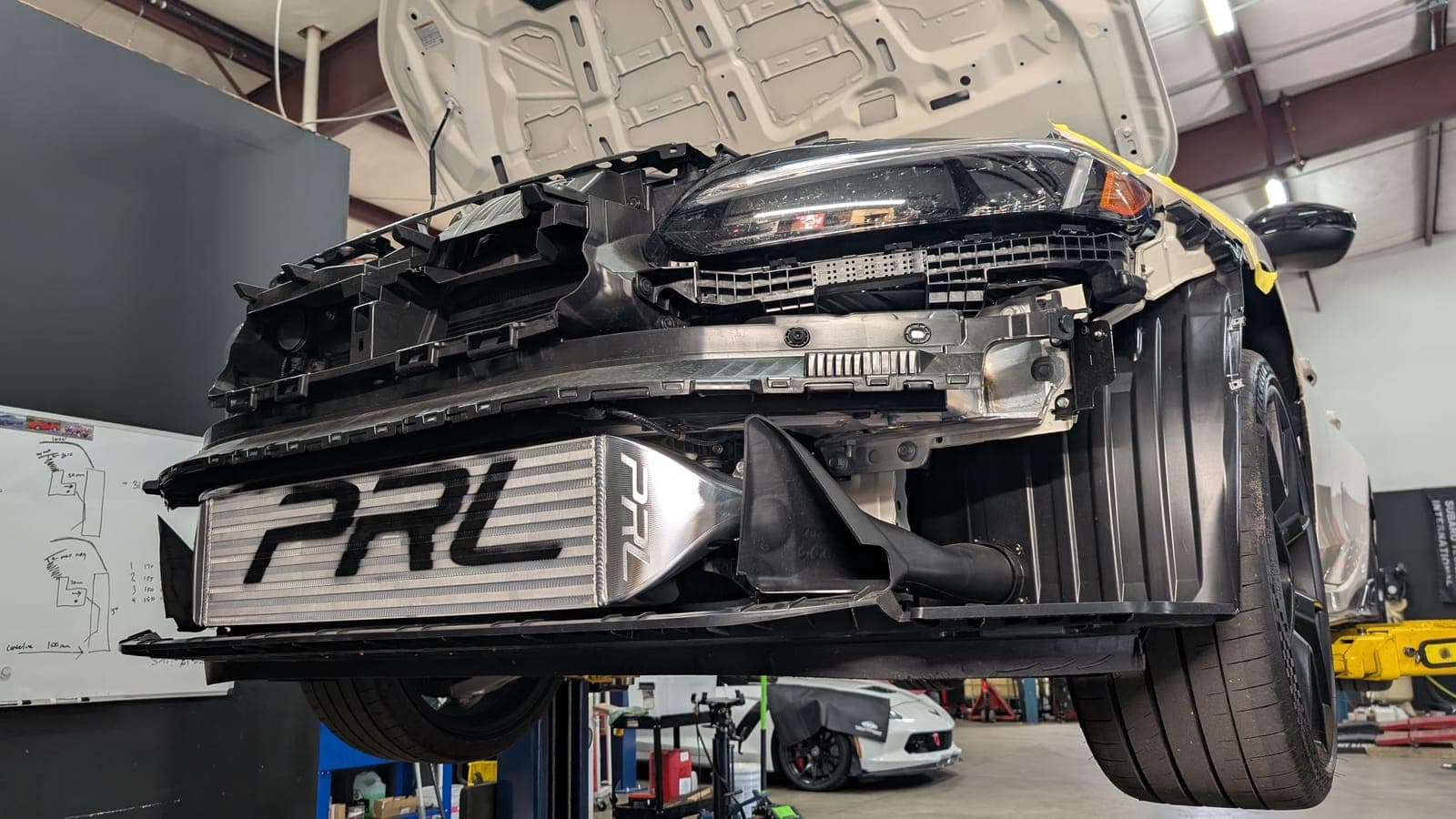 White Honda Civic Type R with the front bumper removed, showing a PRL Motorsports front-mount intercooler being installed inside the Concord shop
