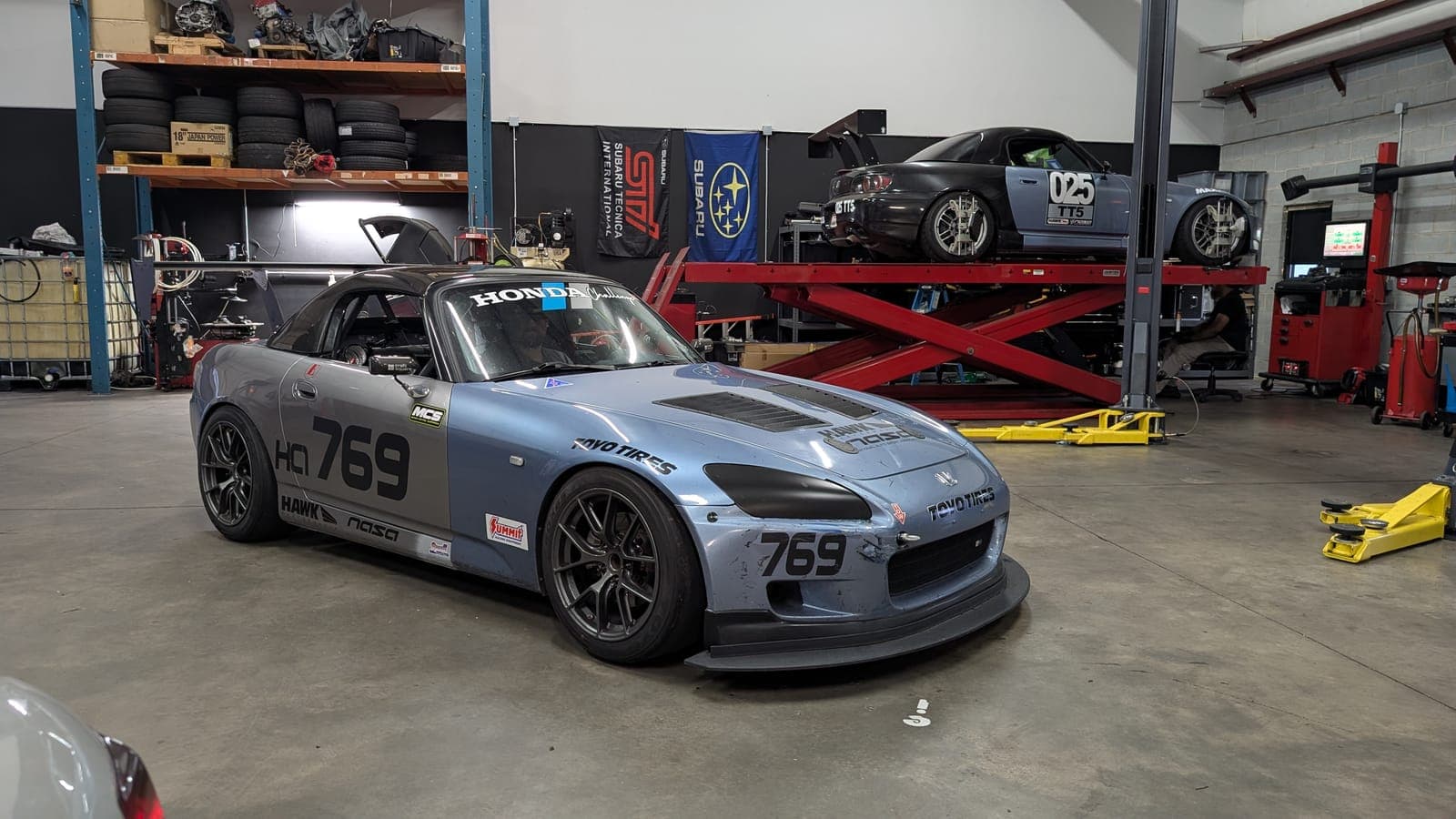 Gray Honda S2000 time attack car, number 769, on the shop floor with another car on the scissor lift behind it