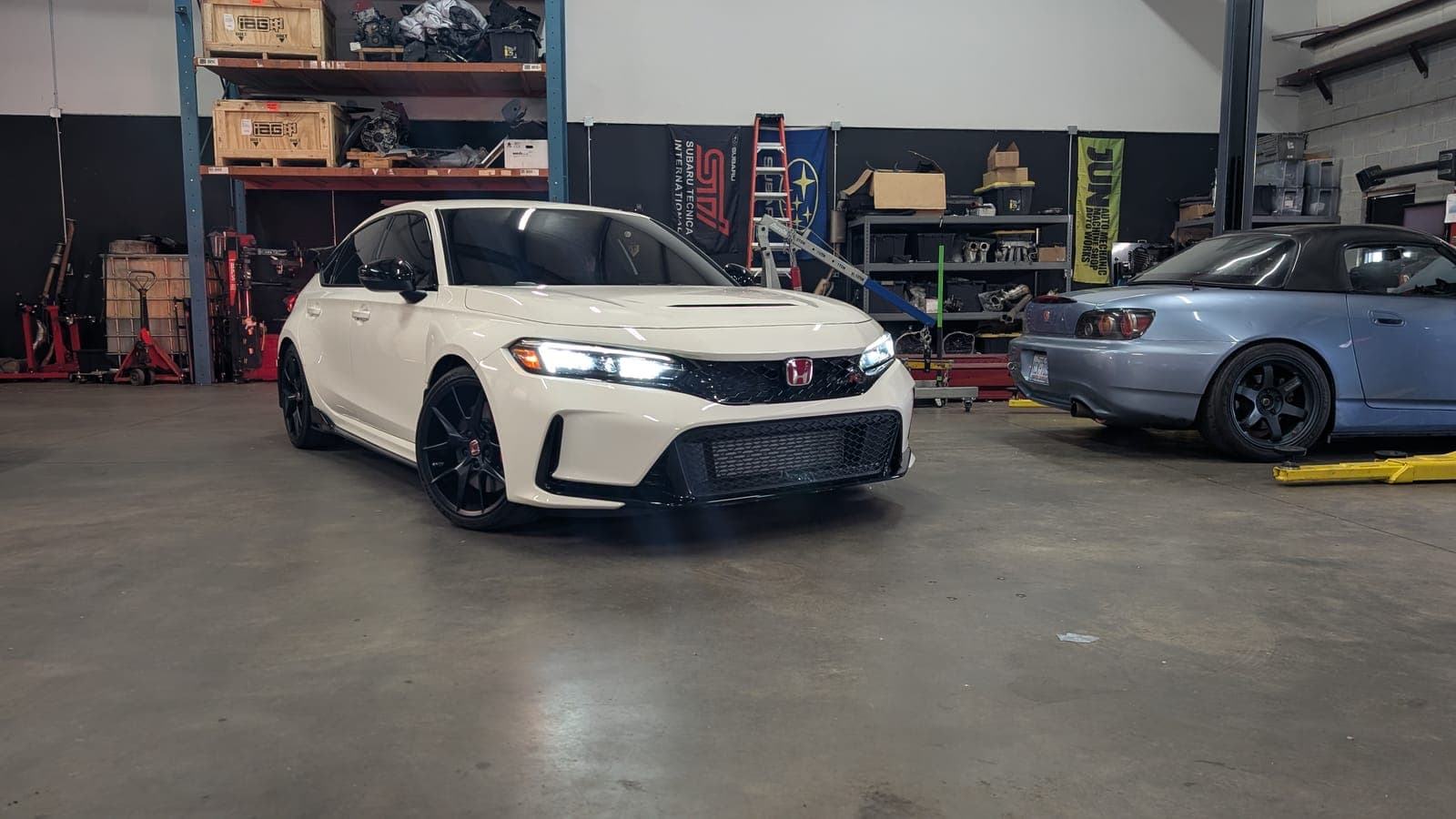 Silver Honda S2000 with a hardtop on the shop floor at Streamline Performance Garage in Concord, NC, with a magenta sedan on the lift behind it