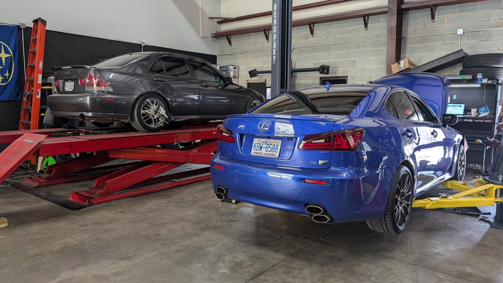 Blue Lexus IS F and a gray Lexus IS 300 on the alignment rack inside the Concord shop