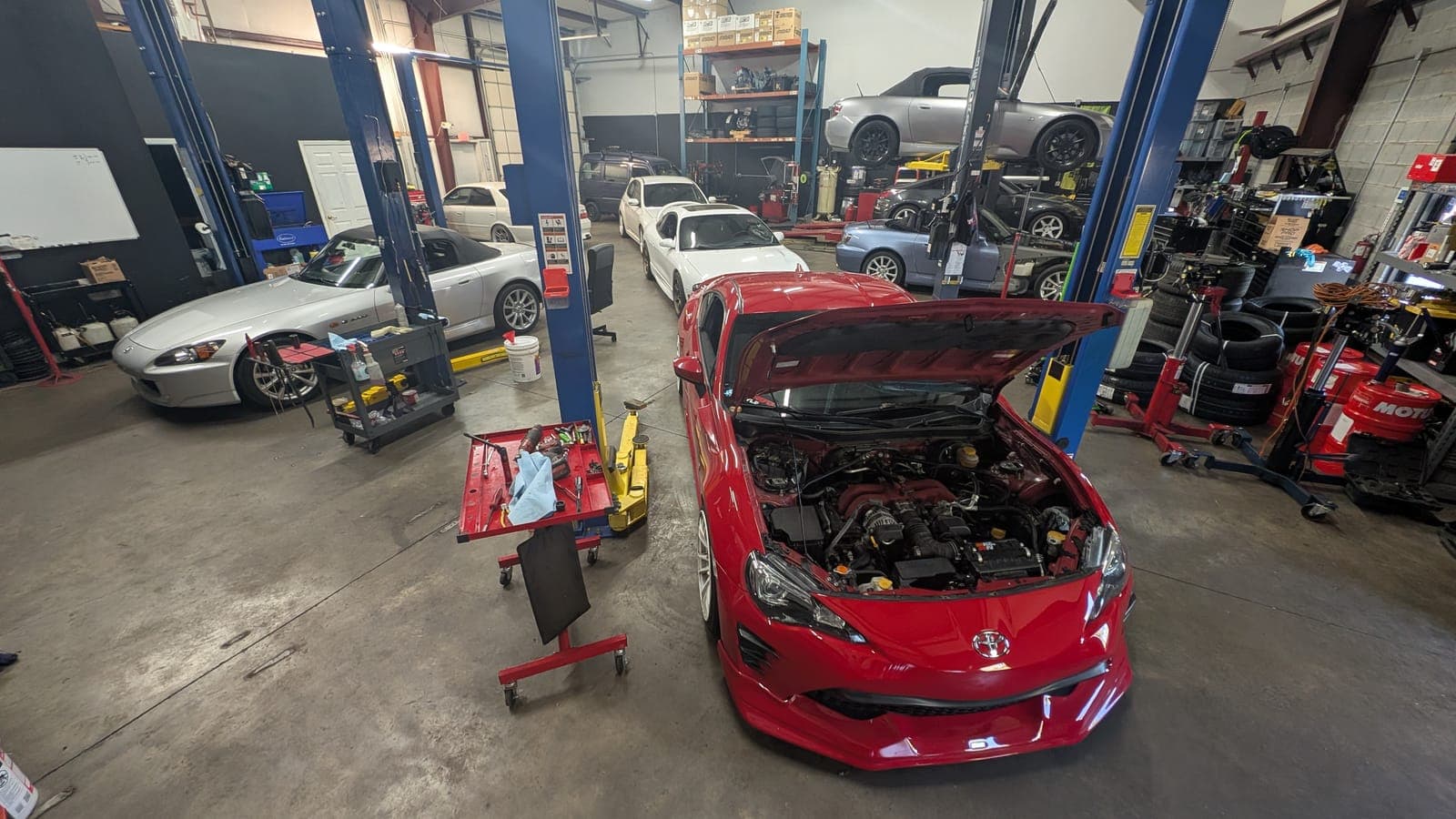 Red Toyota 86 with its hood up between the lifts inside the Streamline Performance Garage shop
