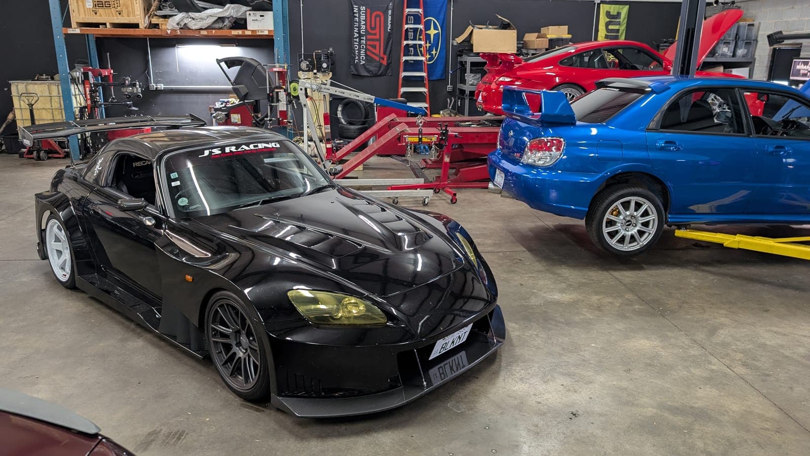 Black wide-body Honda S2000 on the shop floor and a blue bug-eye Subaru Impreza WRX on the lift at Streamline Performance Garage in Concord, NC