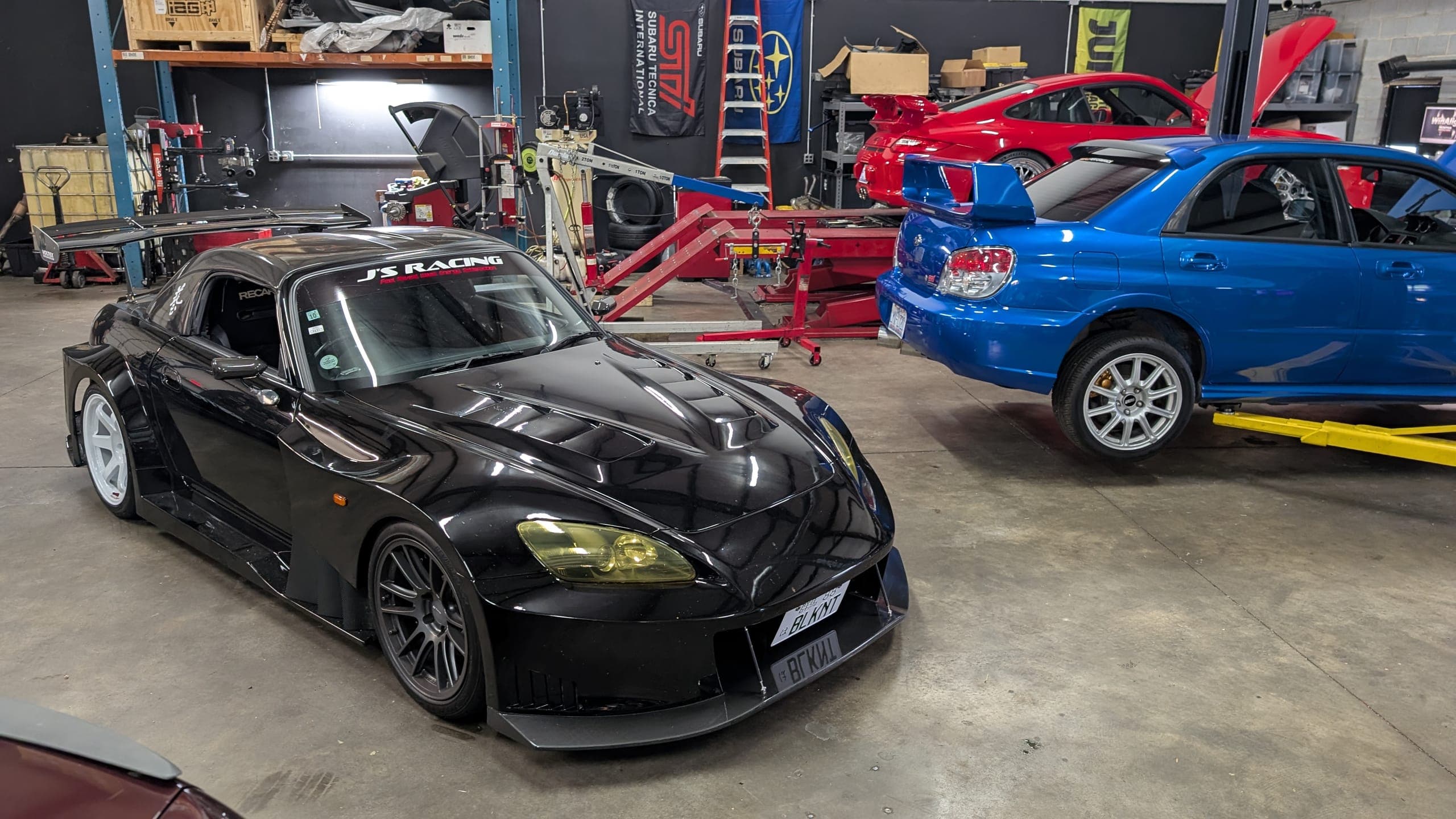 Inside the Streamline Performance Garage shop in Concord, NC: a black wide-body Honda S2000 on the floor and a blue Subaru Impreza WRX on the lift