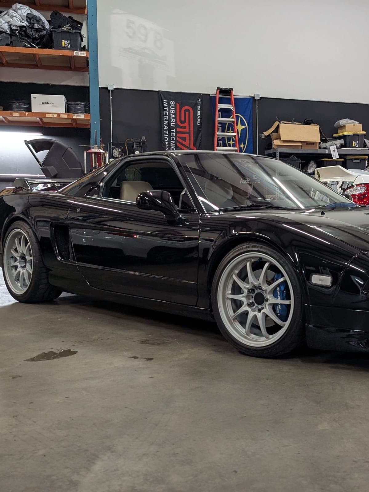 Front three-quarter view of a black first-generation Acura NSX on white wheels inside the Concord shop