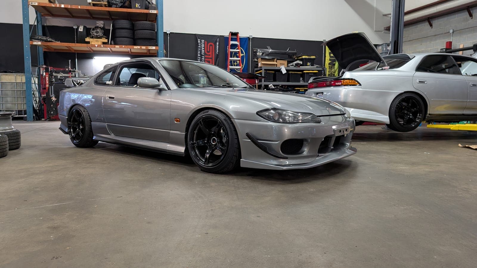 Silver right-hand-drive Nissan Silvia S15 on the shop floor with a white Nissan Skyline behind it